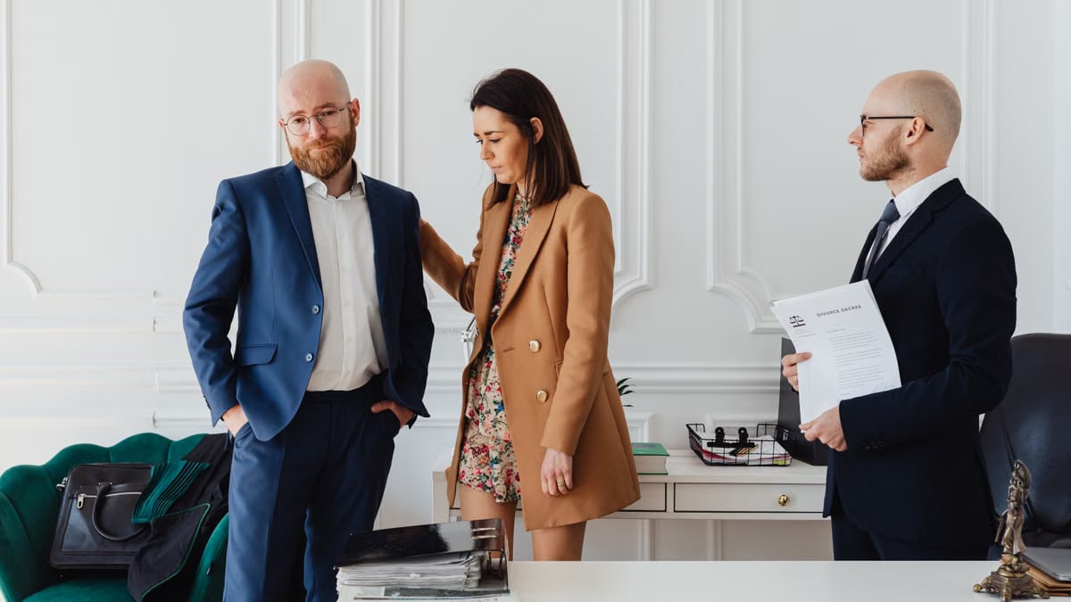 A couple with a lawyer in an office setting, reviewing divorce documents in formal attire.
